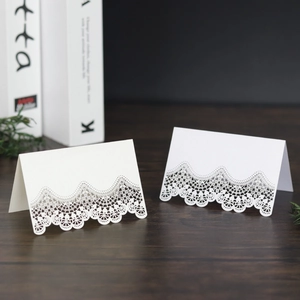 Elegant white laser-cut lace place cards for weddings on a dark wood table background