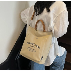 Detail of beige canvas tote with black script text and brown woven handles on stairs