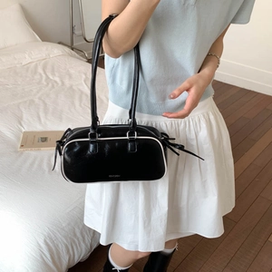 Detail of black bow shoulder bag featuring white contrast trim and sleek patent leather
