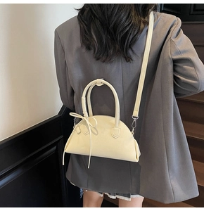 Cream semi-circular crossbody bag shown on a model in a modern urban setting