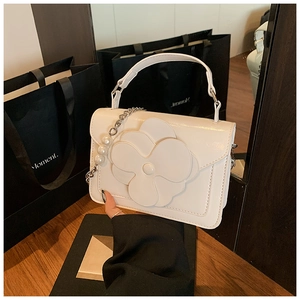 Detail of white matte leather square bag with 3D floral accent and pearl chain strap