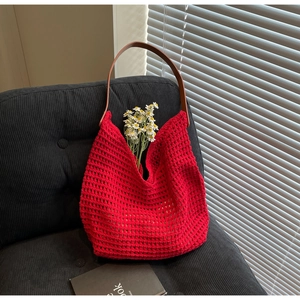 Detail of red hollow crochet tote bag with brown leather handles on a grey sofa