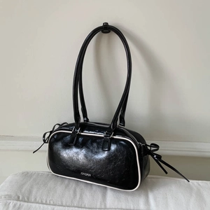 Detail of black glossy shoulder bag with white piping and bow tie side decoration