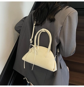 Close-up of a cream crescent shell bag on a model wearing a dark grey suit jacket