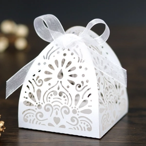 Detail of laser-cut ivory gift box with floral heart patterns and a white ribbon bow