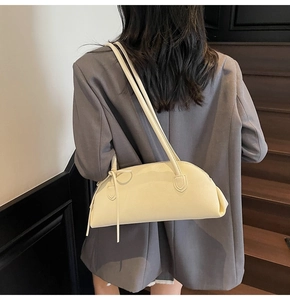 Close-up of cream shell shoulder bag with elegant bow detail on a model in dark blazer