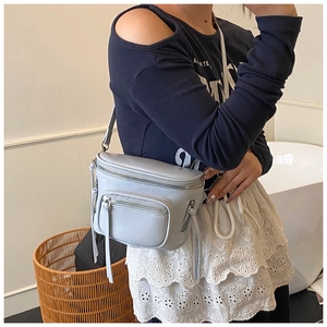 Vue détaillée d'un sac bandoulière en cuir bleu-gris clair avec zips et glands déco