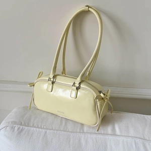 Detailed view of cream yellow baguette bag with glossy texture and bow accents