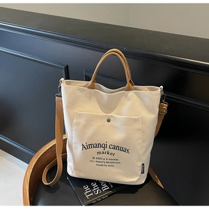Detail of off-white canvas tote bag with brown straps and functional front metal buckle pocket