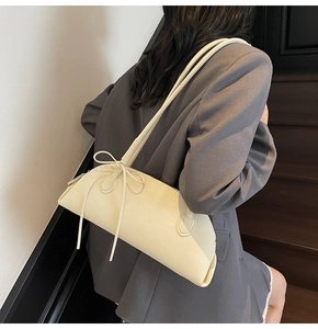 Chic cream bow shoulder bag in textured faux leather styled on model's shoulder