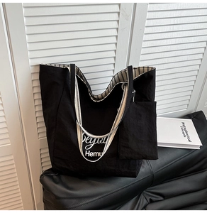 Detail of black canvas tote featuring striped shoulder strap and matching small pouch