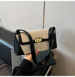 Detailed view of the canvas shoulder bag with black leather trim and gold buckle lock
