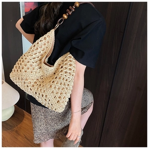 Detail of hollow-out crochet pattern and brown wooden bead shoulder strap on straw tote bag