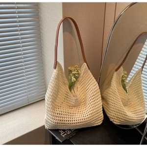 Close-up of a beige hollow knit tote bag with brown leather shoulder strap in sunlight