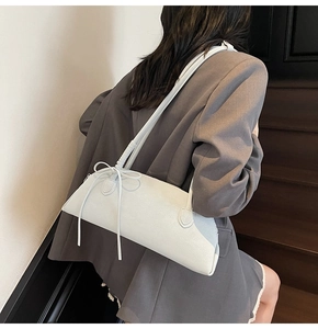 Close-up of a white leather underarm bag with a stylish ribbon bow on a gray blazer