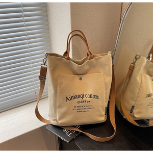 Detail of beige canvas tote bag with brown straps and front pocket under natural sunlight