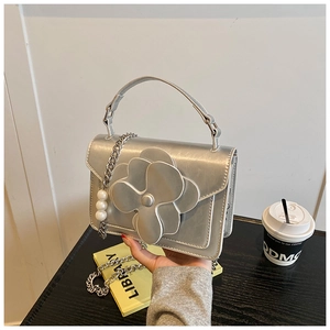 Silver mini bag with 3D floral accent and pearl chain strap held by a hand