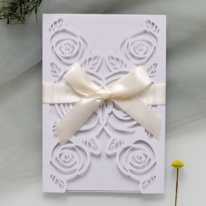 Macro view of laser-cut rose patterns on white wedding invitation with satin ribbon bow