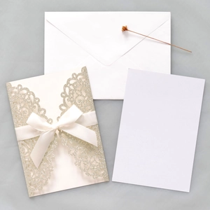 Detail of laser-cut glitter butterfly wedding invitation with cream silk bow and envelopes