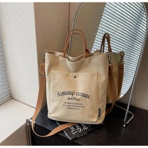 Detail view of beige canvas tote bag featuring brown handles and retro text on front pocket