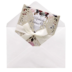 Macro shot of laser-cut glitter wedding invitation with white satin bow and envelope
