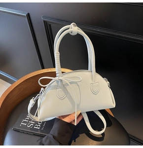 Detail view of grey shell handbag featuring a bow accent and woven top handle detail