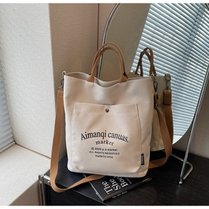 Detailed close-up of beige canvas tote bag with brown straps and functional front snap pocket