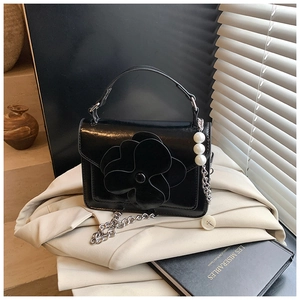 Close-up of black glossy leather bag with 3D camellia flower and pearl charm detail