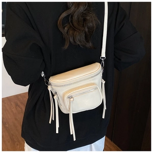 Détail du sac bandoulière crème minimaliste avec zips argentés et pompons en cuir