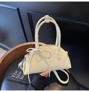 Detail of cream white shell bag with lychee texture, bow decor, and slim strap