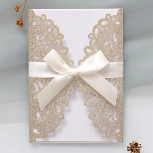 Macro shot of glitter champagne gold laser-cut wedding invitation with a white satin bow
