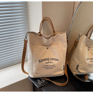 Detail of beige canvas tote bag featuring brown leather straps and outer pocket