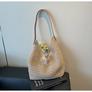 Close-up of beige hollow knit tote bag with brown leather strap on black leather sofa