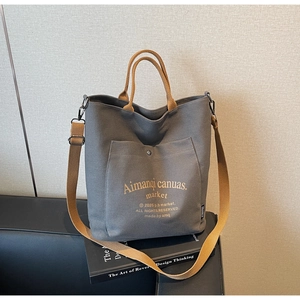 Detailed close-up of a large grey canvas tote bag with brown woven straps and logo pocket
