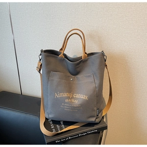 Detail of grey canvas tote bag with brown woven straps and front pocket closure