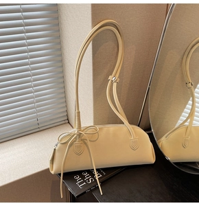 Detailed side view of cream baguette bag with decorative bow and slim shoulder strap