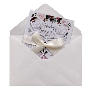 Macro detail of laser-cut rose invitation with cream ribbon and floral inner card