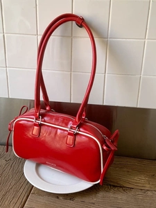 Red faux leather bow shoulder bag with white piping and silver metal buckles