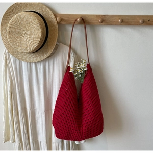 Detail of red crochet knit tote bag with brown leather straps in a cozy aesthetic setting
