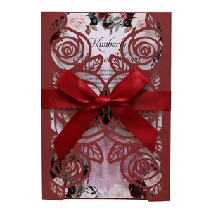 Detail of laser-cut burgundy rose pattern on wedding invitation with red satin bow