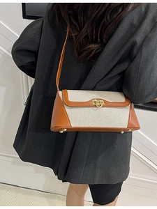 Canvas shoulder bag with brown leather trim and gold hardware worn by a model in a suit