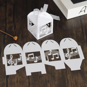 Detail of white laser-cut musical note candy box with silk ribbon and flat layout