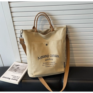 Detail of large canvas tote bag with brown leather handles and metal buckle pocket