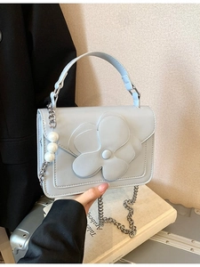 Elegant light blue crossbody bag with floral detail and pearl chain strap on book