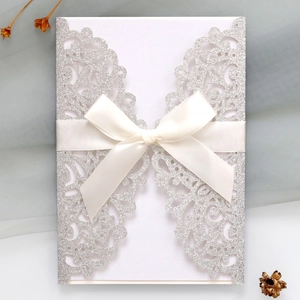 Detail of silver glitter laser-cut wedding invitation with elegant satin bow and inner card
