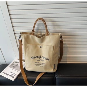 Detail of a beige canvas tote bag with brown handles and front pocket on a black bench