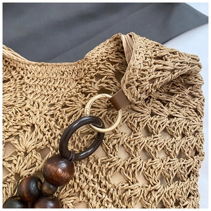 Detail of woven straw tote with wooden beads, golden metal rings and leather accents