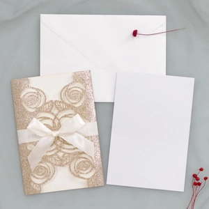 Close-up of laser-cut champagne glitter rose invitation with white silk ribbon bow