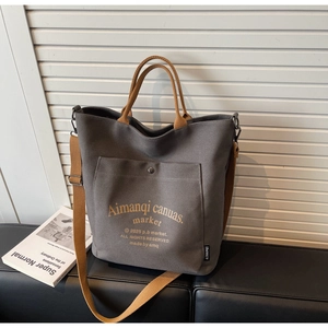 Detail view of large canvas tote bag showing front snap pocket and dual-color shoulder straps
