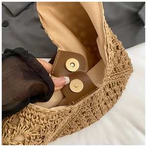 Detail of magnetic snap closure on a woven straw tote bag with leather trim and inner lining